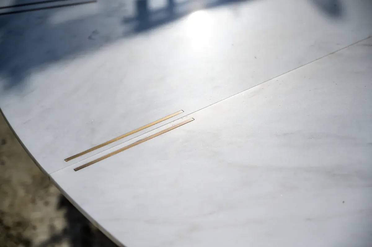 Piano di un tavolo in marmo bianco con inserti in ottone incassati nella superficie